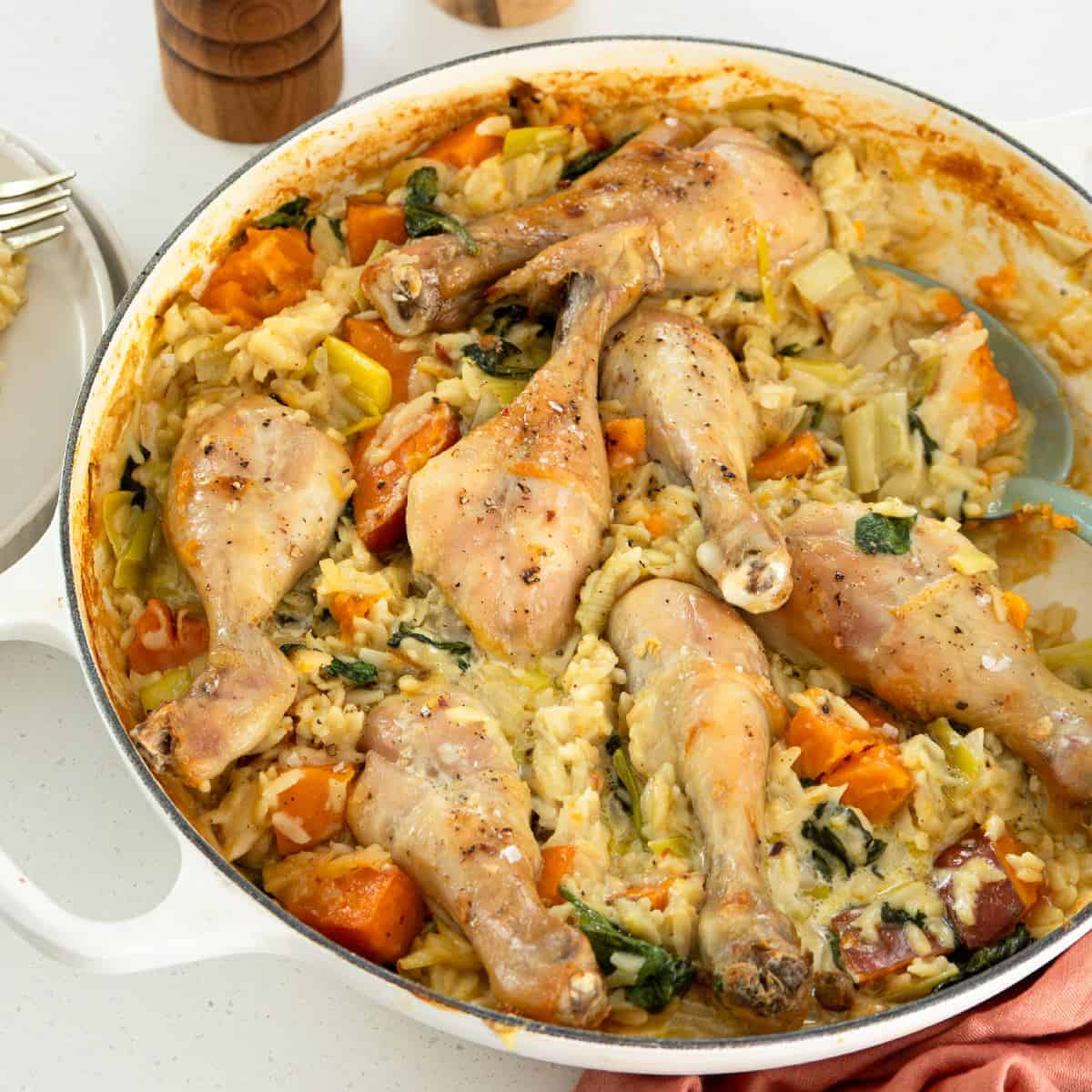 One pot chicken leek and orzo bake Baked chicken drumsticks on a bed of creamy rice with vegetables in a white baking dish.