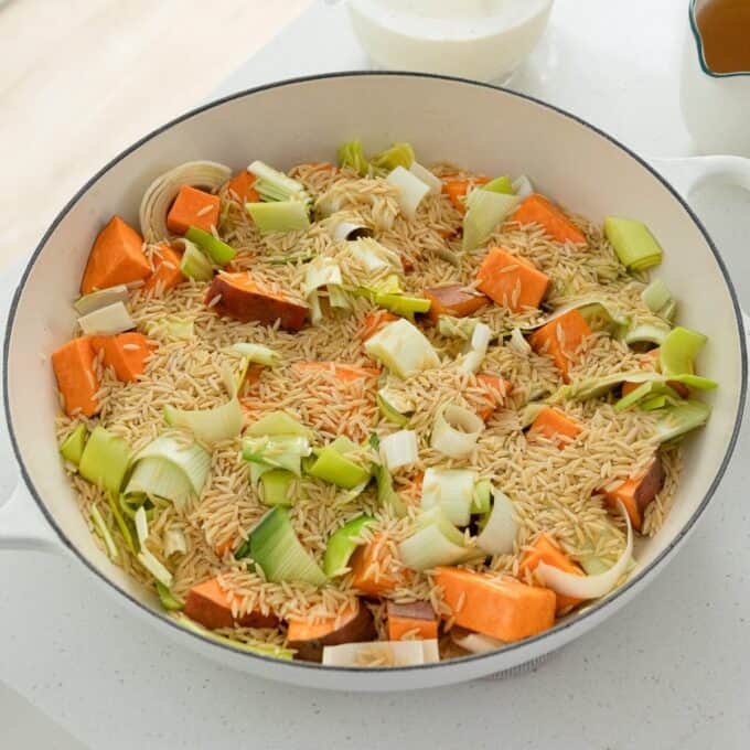 One Pot Chicken, Leek and Orzo Bake A white pan filled with uncooked brown rice, chopped sweet potatoes, and sliced leeks sitting on a kitchen counter.