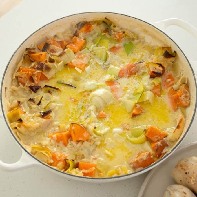 One Pot Chicken, Leek and Orzo Bake A white pot filled with a baked dish containing chunks of sweet potatoes, leeks, and a creamy yellow sauce on a white countertop.