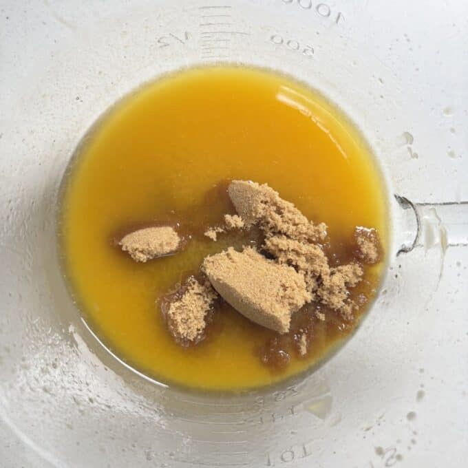 Gluten Free Bumper Bars A glass measuring cup containing melted butter and brown sugar on a white surface.