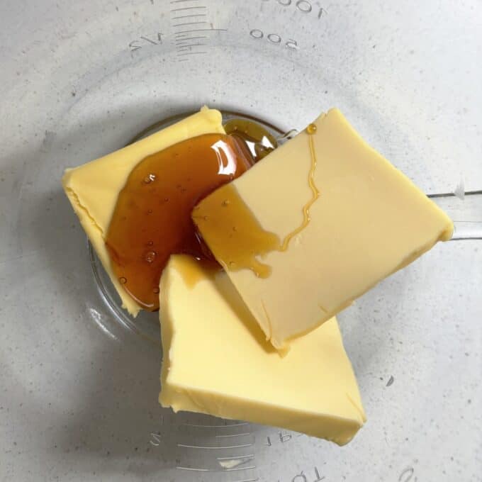 Gluten Free Bumper Bars Three slices of butter and a drizzle of honey sit in a clear glass bowl on a light-colored surface.