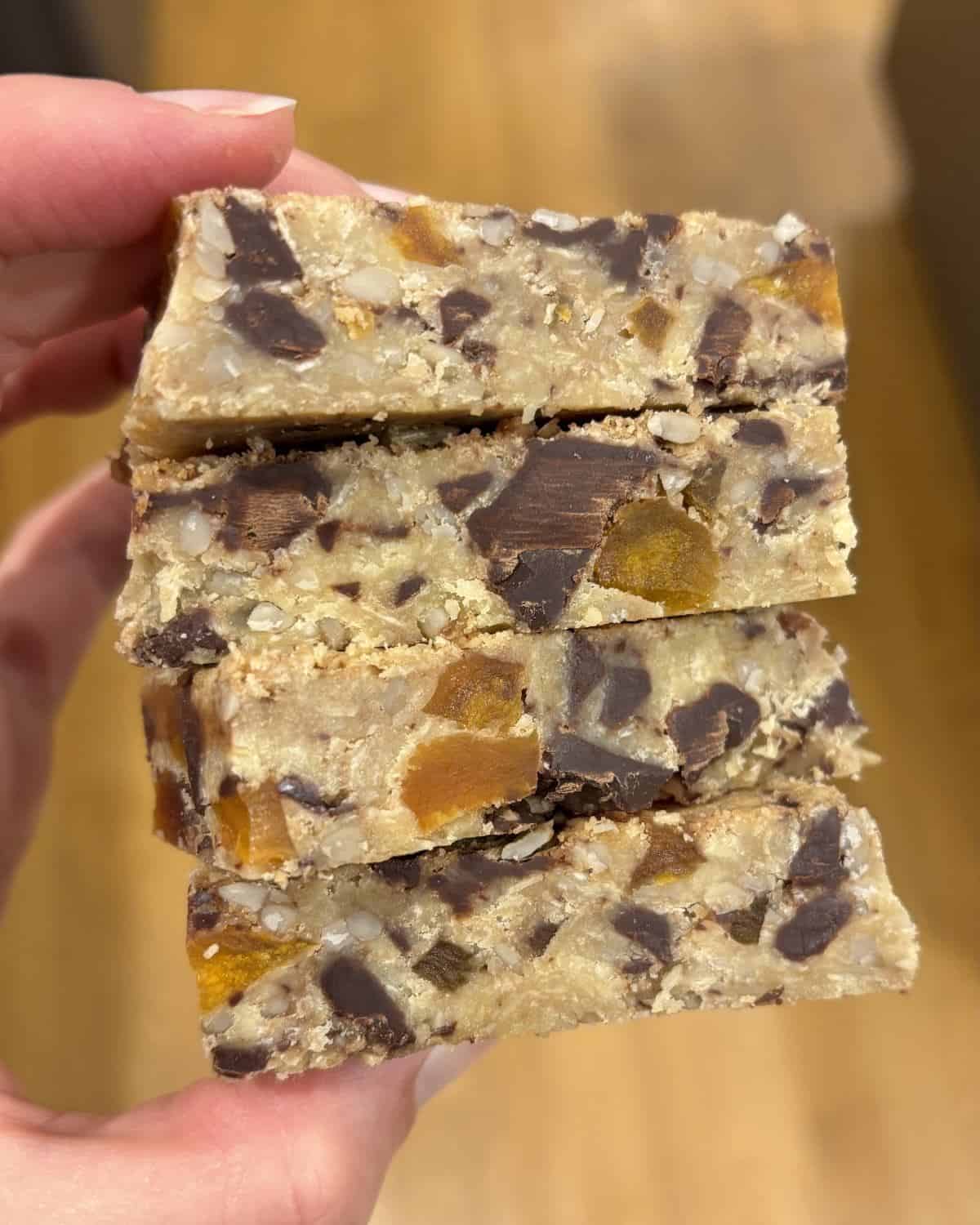 Gluten Free Bumper Bars A hand holds four stacked homemade granola bars with visible chunks of chocolate and dried fruit.