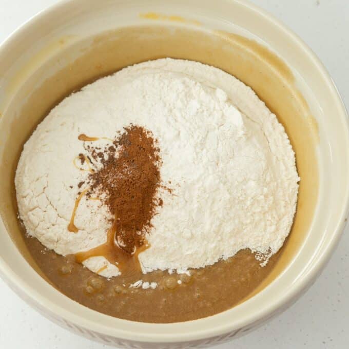 Hot Cross Blondies A mixing bowl with flour, cinnamon, vanilla extract, and a brown liquid batter, ready to be mixed together.