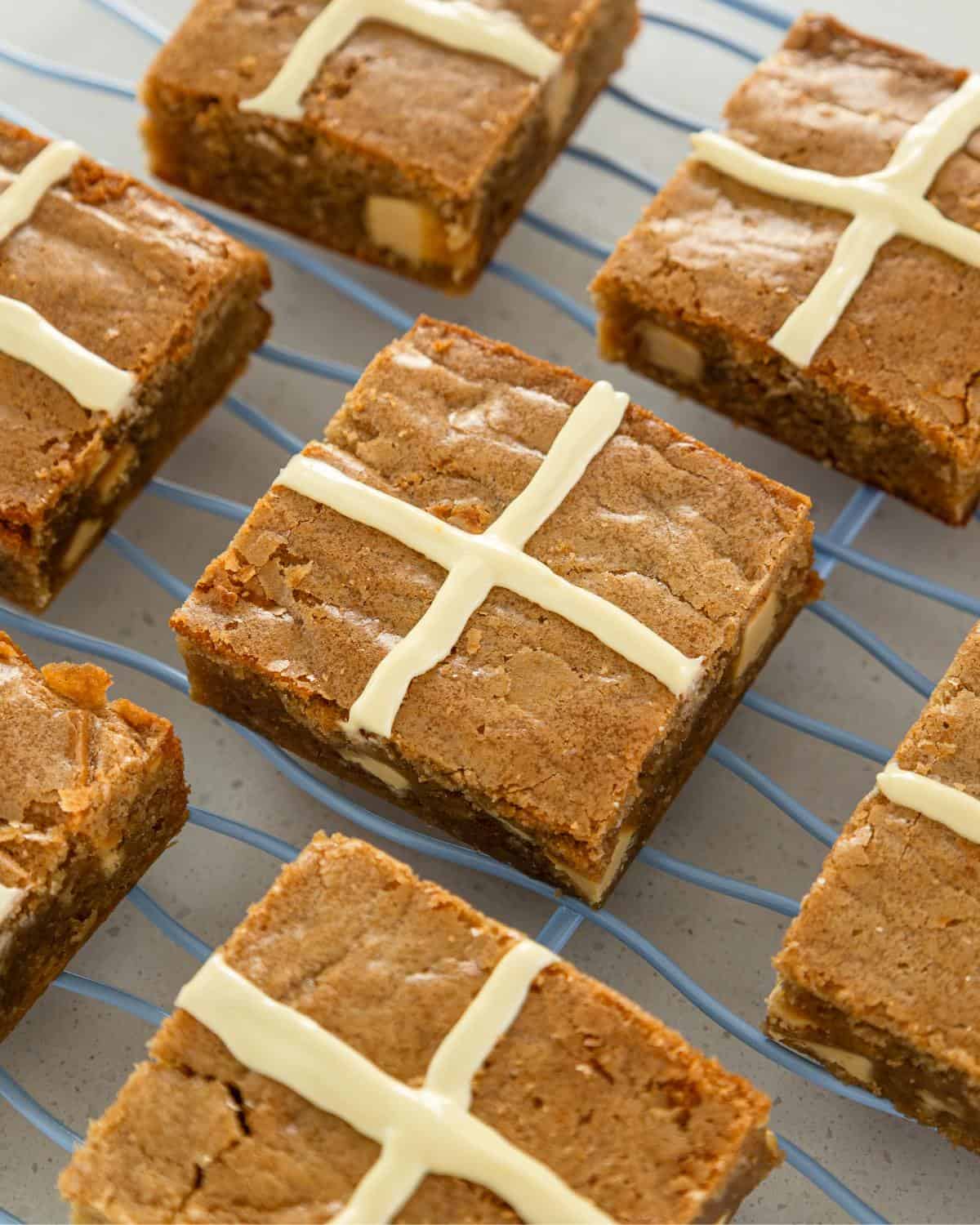 Several blondie squares with white chocolate cross decorations are cooling on a blue wire rack.