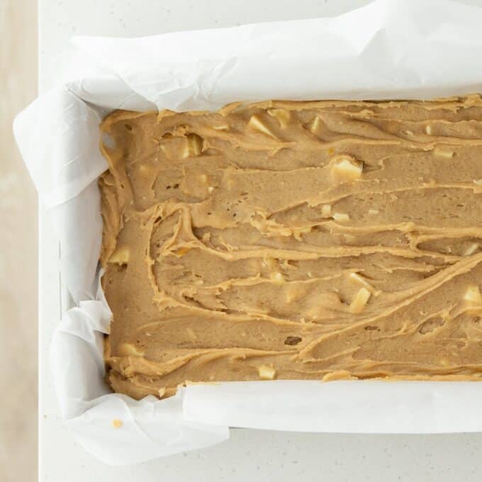 Hot Cross Blondies Rectangular baking pan lined with parchment paper, filled with raw batter containing small chunks, ready to be baked.