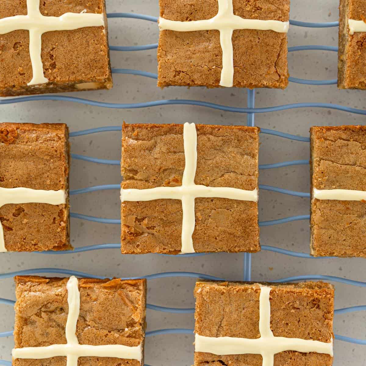 Hot Cross Blondies Nine square blondie bars with white icing crosses on top, arranged in a grid pattern on a wire cooling rack.