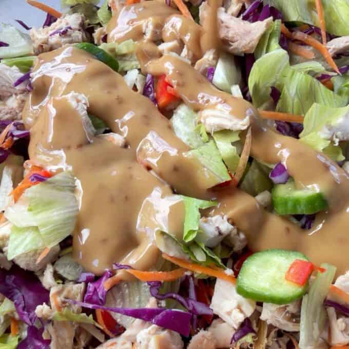 Rotisserie Chicken Salad Chopped salad with lettuce, carrots, red cabbage, cucumbers, chicken pieces, and a generous drizzle of creamy brown dressing on top.