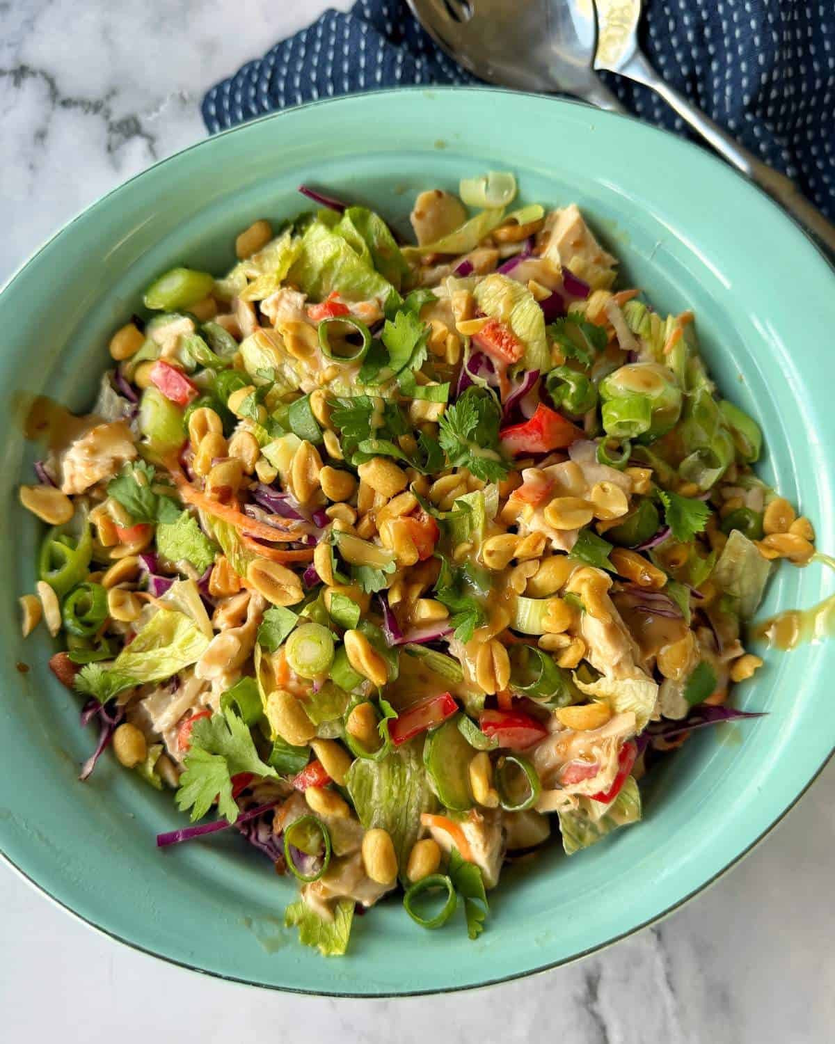 Rotisserie Chicken Salad A bowl of salad with lettuce, shredded cabbage, red peppers, green onions, cilantro, peanuts, and a creamy dressing, served on a green plate.