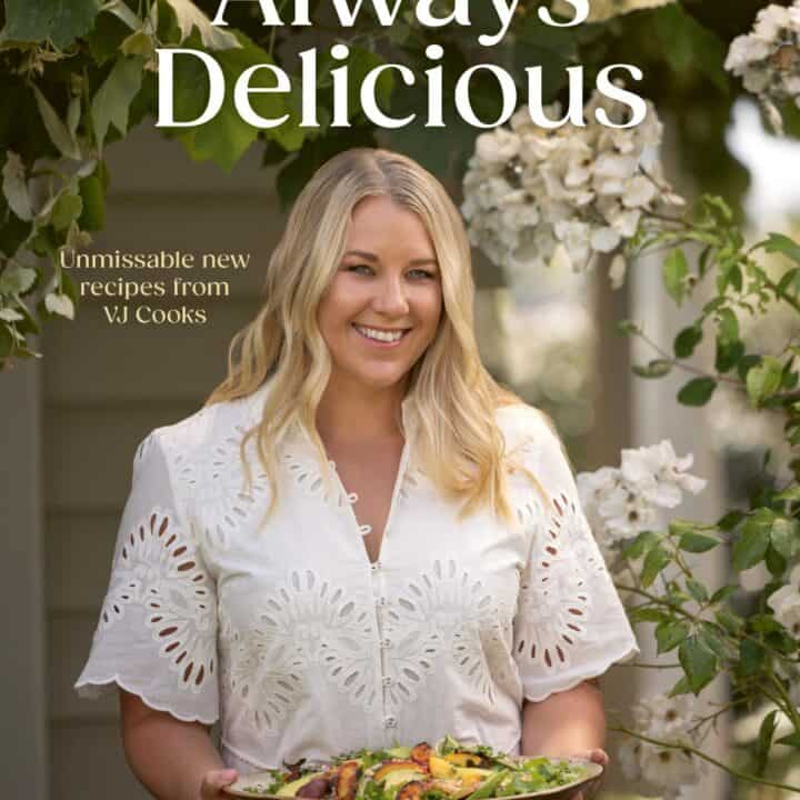Woman in a white dress holding a platter of food stands outdoors under flowering branches. Text reads: Always Delicious, Unmissable new recipes from VJ Cooks, Vanya Insull..