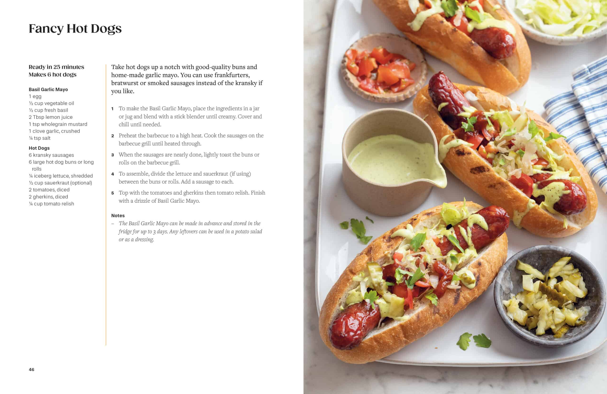 Three grilled hot dogs in buns topped with cabbage slaw are arranged on a tray next to a bowl of green basil garlic mayo and a striped napkin. Recipe instructions appear on the left.