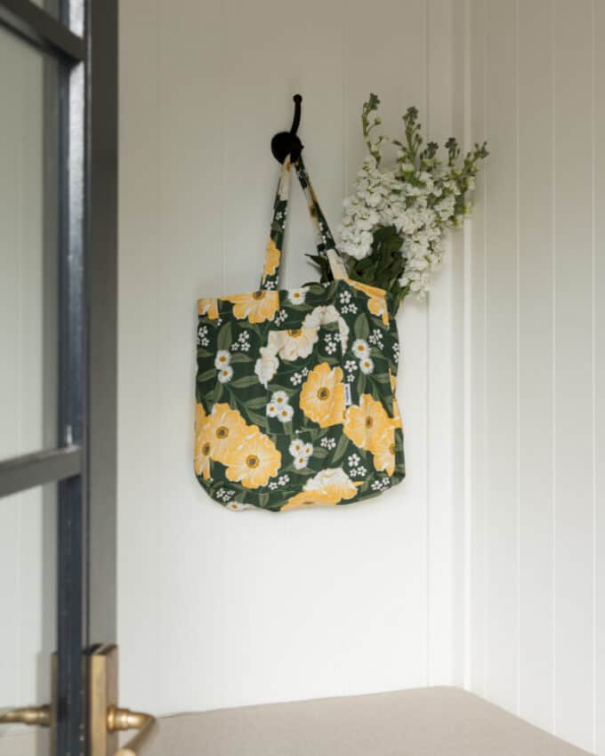 A floral-patterned tote bag with yellow and white flowers hangs on a hook; white flowers are visible sticking out of the bag.