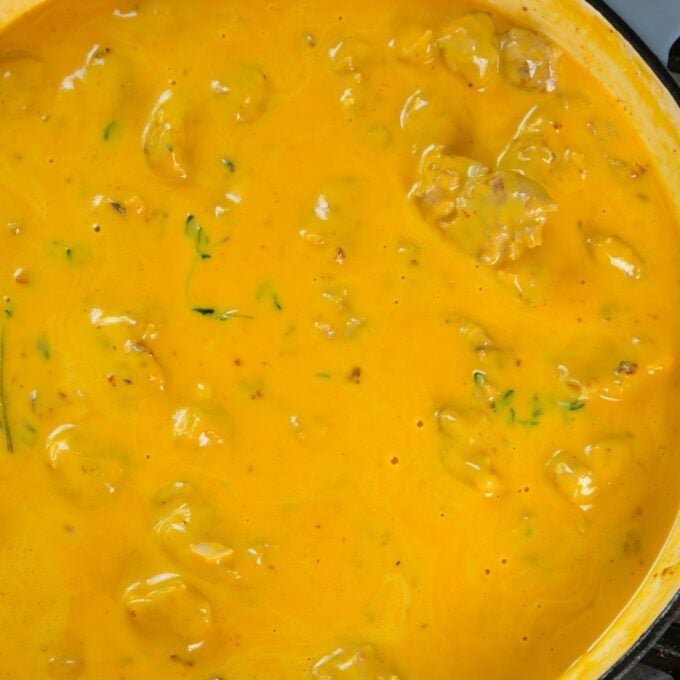 Creamy Pumpkin and Sausage Gnocchi A close-up of yellow cheese sauce with ground beef and bits of green herbs in a pan.
