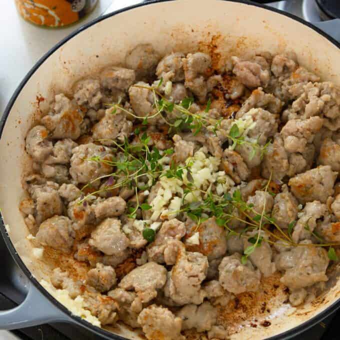 Creamy Pumpkin and Sausage Gnocchi Chunks of browned sausage cook in a pan with chopped garlic and sprigs of fresh thyme on top.