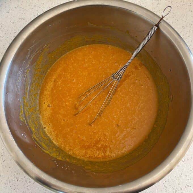 Pumpkin Spice Cake A metal mixing bowl with orange batter and a metal whisk resting inside, on a light-colored countertop.