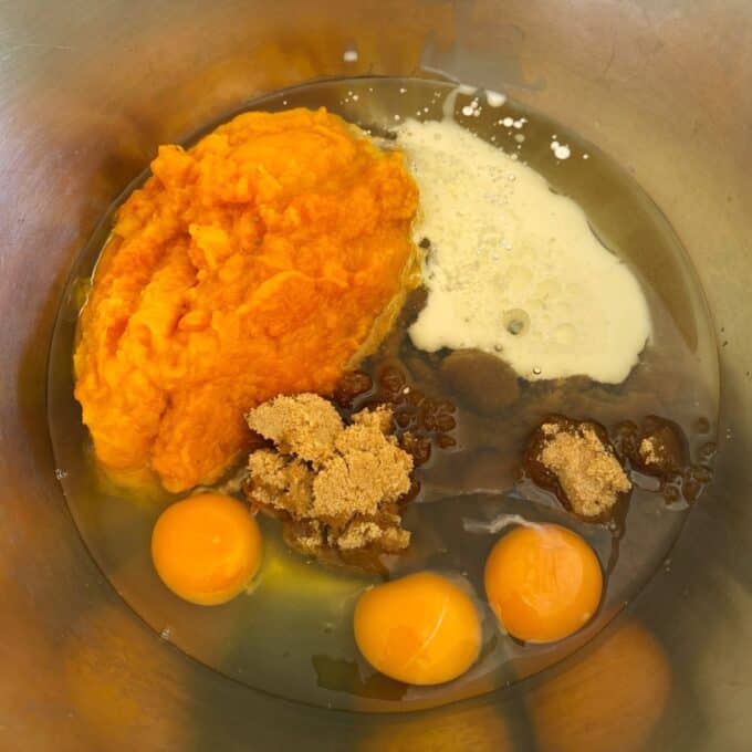 Pumpkin Spice Cake A metal bowl with pumpkin puree, three raw eggs, brown sugar, vanilla extract, and milk, ready to be mixed for baking.
