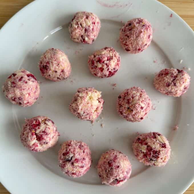 White Chocolate and Raspberry Tim Tam Balls Twelve pink and white cheese balls with visible berry pieces are arranged on a white plate, viewed from above.