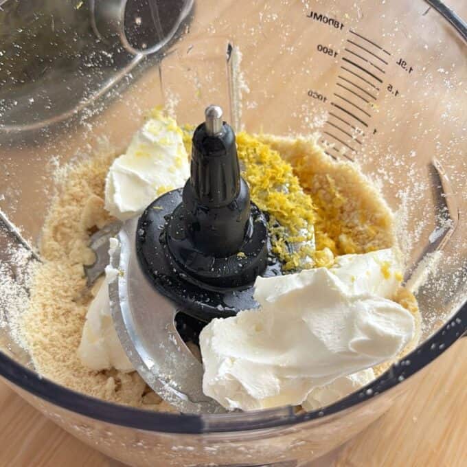 White Chocolate and Raspberry Tim Tam Balls Ingredients including cream cheese, lemon zest, and flour are in a food processor bowl, ready to be mixed.
