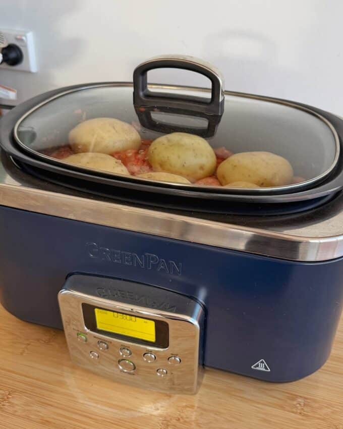 Slow Cooker Chicken Ragu A slow cooker labeled GreenPan is cooking whole potatoes and other ingredients under a glass lid, with the digital display showing 08:00.