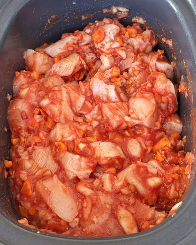 Slow Cooker Chicken Ragu Raw chicken pieces mixed with tomato sauce and chopped vegetables in a slow cooker, ready to be cooked.