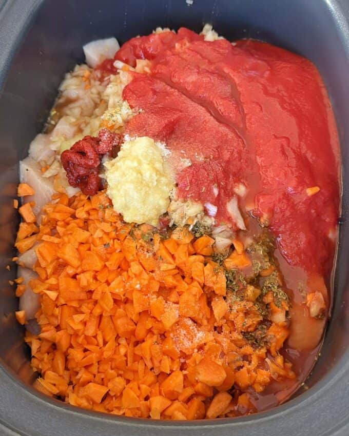 Slow Cooker Chicken Ragu Chopped carrots, onions, tomato puree, tomato paste, minced garlic, and seasonings are placed together in a slow cooker before mixing.
