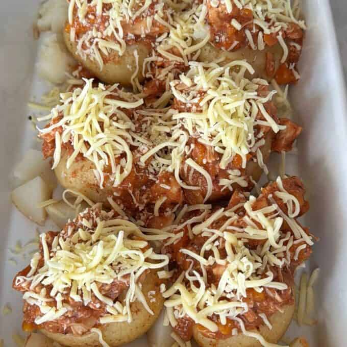 Slow Cooker Chicken Ragu Round rolls topped with shredded chicken in red sauce and grated cheese, arranged in a white baking dish, ready to be baked or served.