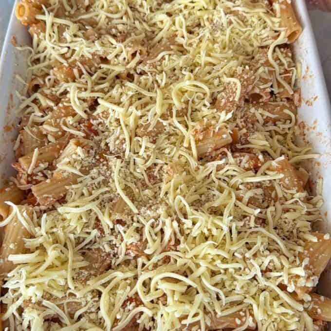 Slow Cooker Chicken Ragu Unbaked pasta casserole in a white dish, topped with shredded cheese and breadcrumbs.