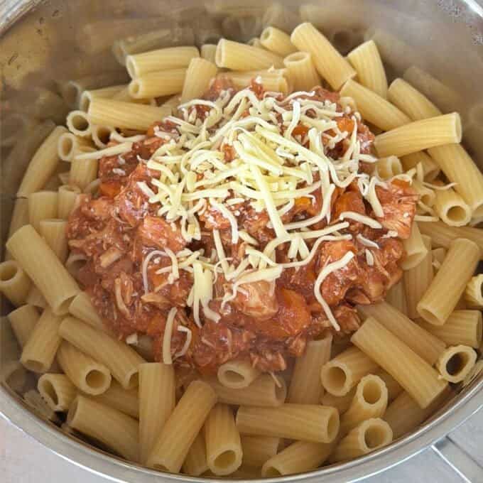 Slow Cooker Chicken Ragu A pot filled with cooked rigatoni pasta, topped with a tomato-based meat sauce and a sprinkle of shredded cheese in the center.