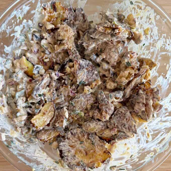 Smashed Potato Salad A clear bowl filled with roasted potato salad mixed with creamy dressing, chopped herbs, and vegetables.