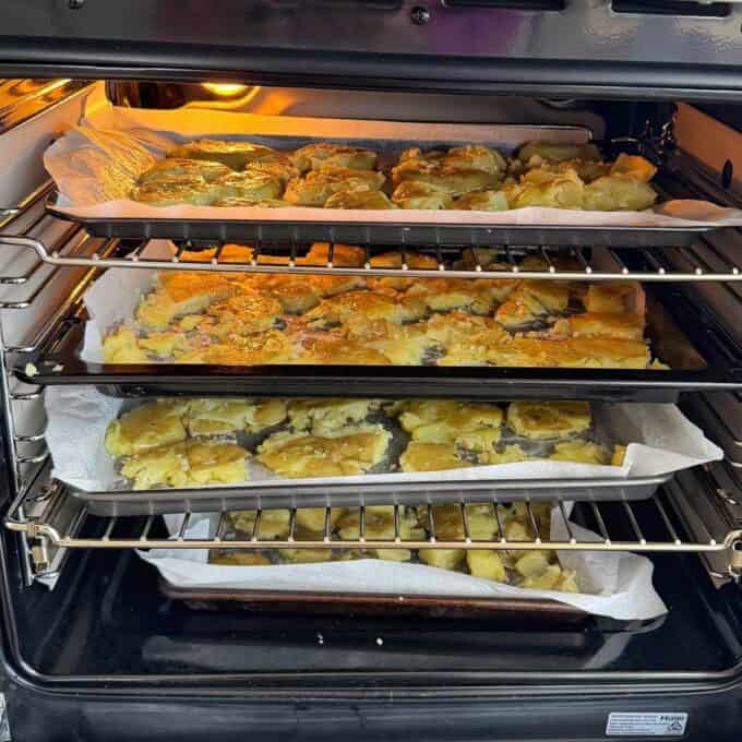 Smashed Potato Salad Three trays of baked goods on parchment paper are stacked inside an oven, with the top tray appearing more golden-brown than the two trays below it.