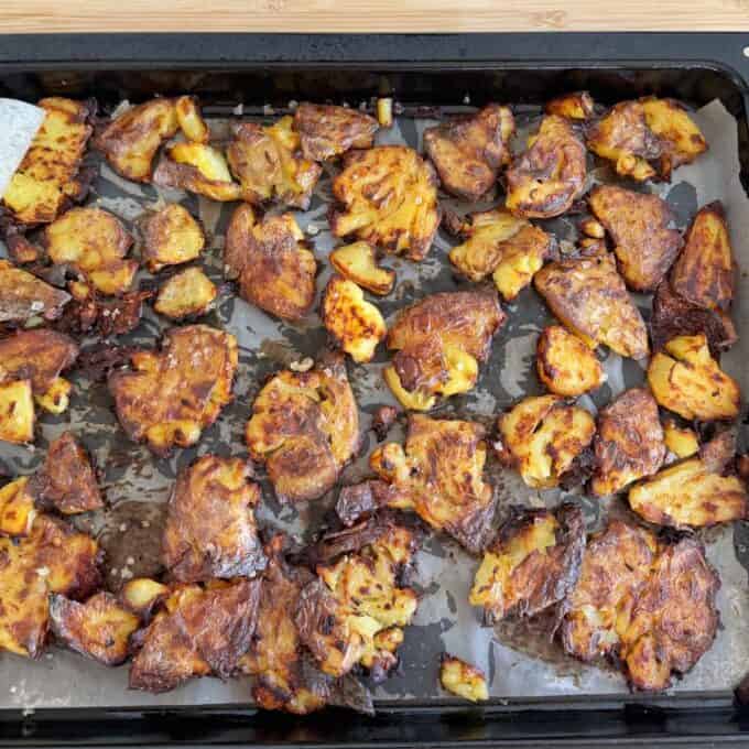 Smashed Potato Salad Sheet pan with roasted smashed potatoes on parchment paper, golden brown and crispy, arranged in a single layer.