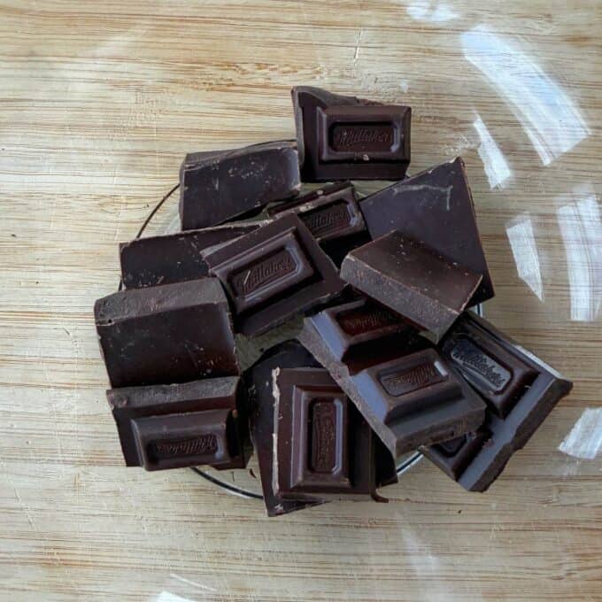 Tim Tam Cheesecake Balls A glass bowl filled with pieces of dark chocolate sits on a wooden surface.