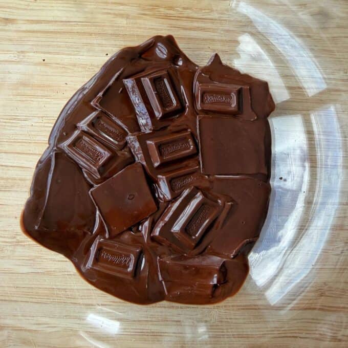 Tim Tam Cheesecake Balls Partially melted chocolate squares on a wooden surface inside a clear glass bowl.