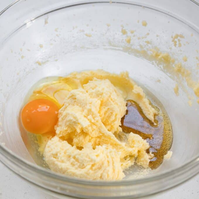 Tinned Plum Sponge Pudding Clear glass bowl with softened butter, sugar, a cracked egg, and vanilla extract, about to be mixed together as part of a recipe.