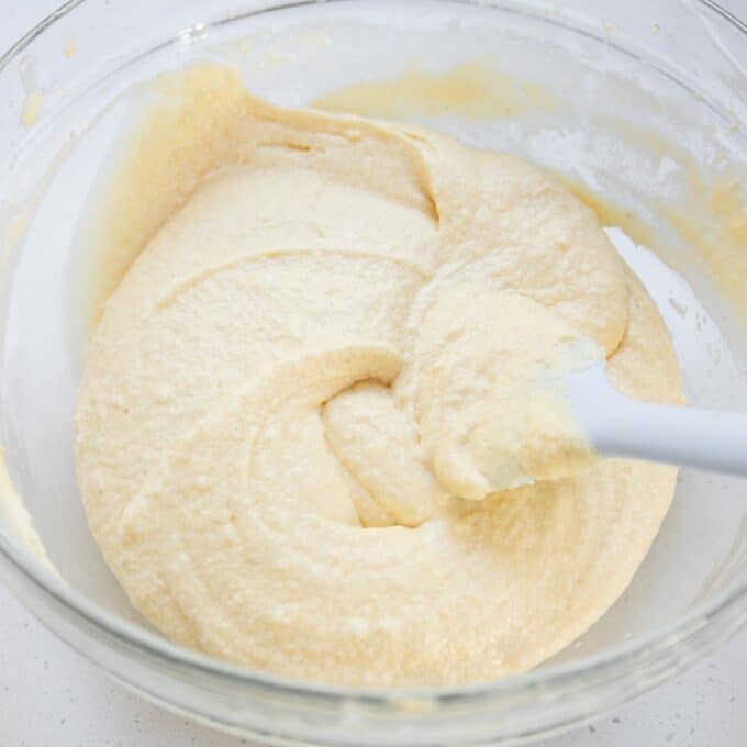 Tinned Plum Sponge Pudding A glass bowl containing pale yellow cake batter being mixed with a white spatula.