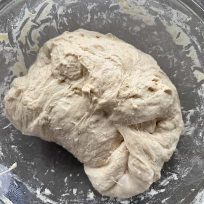 XL No-Knead Focaccia A ball of unbaked bread dough sits in a glass mixing bowl, showing a sticky and slightly lumpy texture.