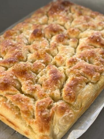 A golden-brown, rectangular loaf of homemade focaccia bread topped with coarse salt, resting on parchment paper.