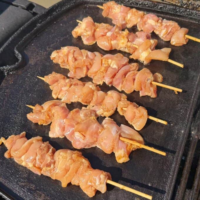Chicken Yakitori Skewers Six uncooked chicken skewers are arranged in rows on a hot griddle or grill, ready to be cooked.