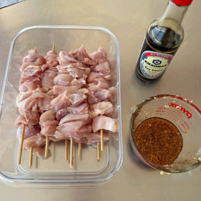Chicken Yakitori Skewers Raw chicken skewers in a container, a bottle of Kikkoman soy sauce, and a measuring cup with marinade on a counter.