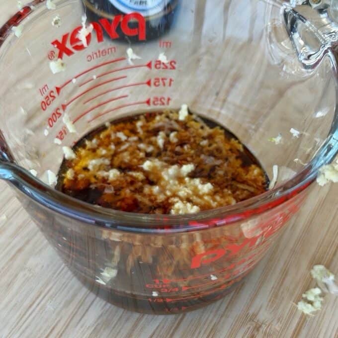 Chicken Yakitori Skewers A glass measuring cup on a wooden surface contains a mixture of soy sauce, minced garlic, and seasonings.