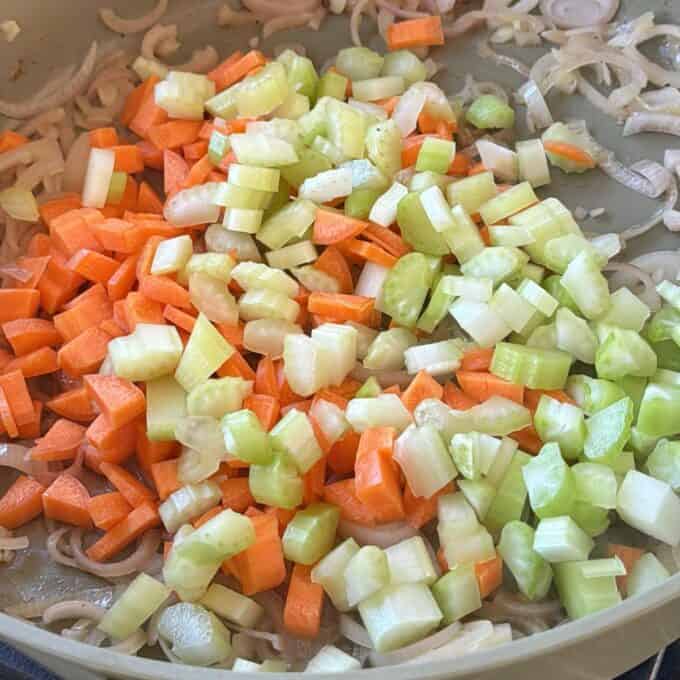 Beef Cheeks with Red Wine Sauce Chopped carrots, celery, and onions cooking in a pan, with the vegetables partly sautéed and not yet fully softened.