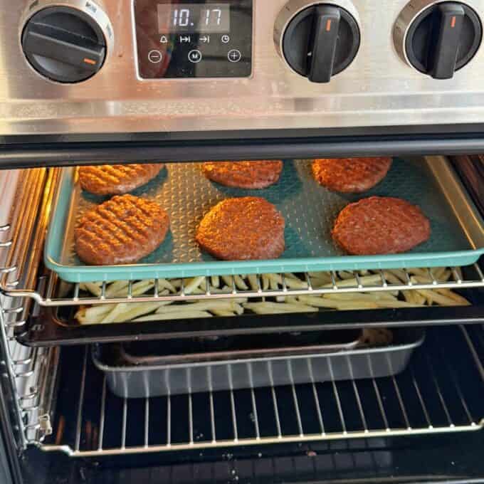 Big Mac Burger Bowls Six burger patties cook on a baking tray in the oven, with a tray of fries baking below them. The oven timer reads 10:17.