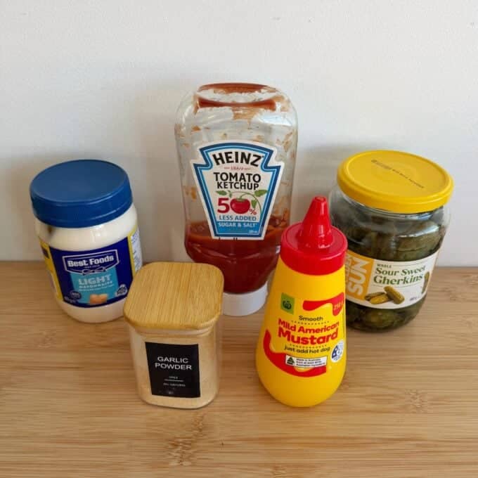 Big Mac Burger Bowls Five condiments on a wooden surface: mayonnaise, ketchup, garlic powder, mild American mustard, and a jar of sour sweet gherkins.