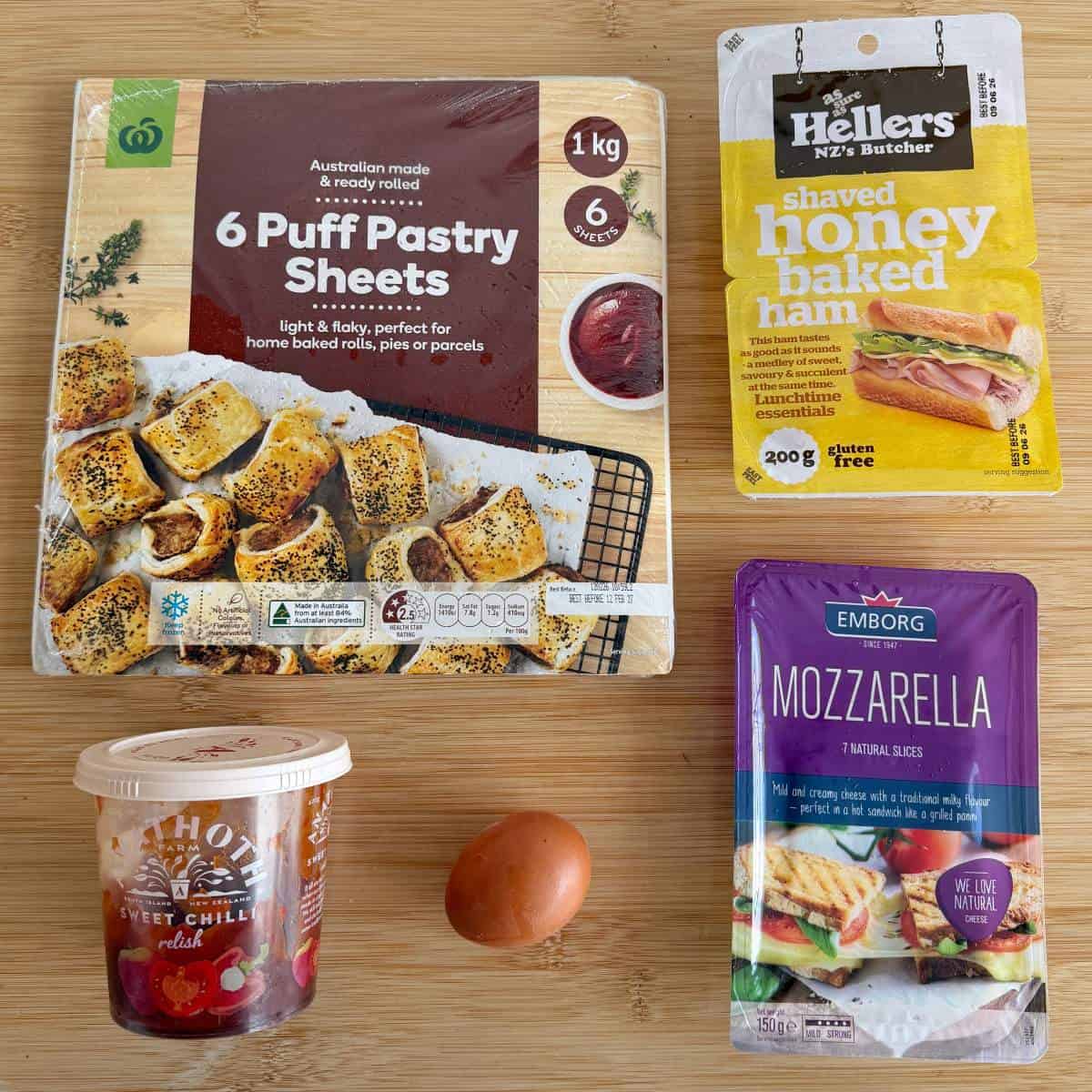 Ham and Cheese Puff Pastry Croissants Four ingredients—puff pastry sheets, honey baked ham, grated mozzarella, and sweet chili relish—plus a single egg are arranged on a wooden surface.