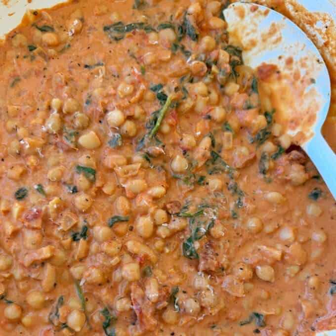 Marry Me Chickpeas and Beans Close-up of a creamy lentil and spinach curry with a white serving spoon partially visible on the right side.