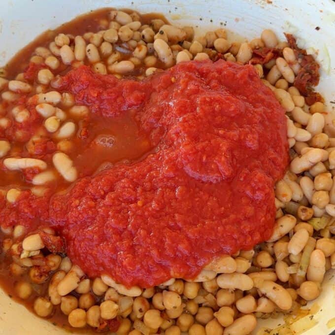 Marry Me Chickpeas and Beans White beans mixed with herbs and spices in a pan, topped with a layer of tomato sauce.