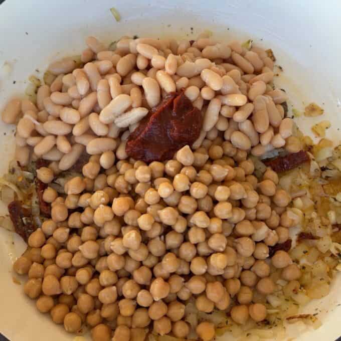 Marry Me Chickpeas and Beans White beans, chickpeas, chopped onions, and sun-dried tomatoes are mixed together in a white bowl.