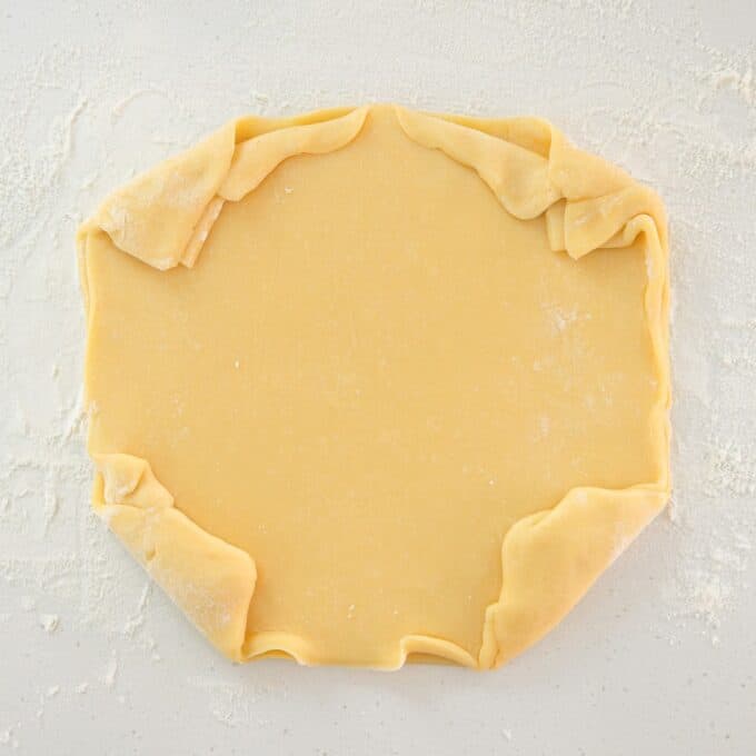 Rhubarb and Apple Galette Rolled out pastry dough on a floured surface with edges folded inward, forming an uneven rectangular shape.