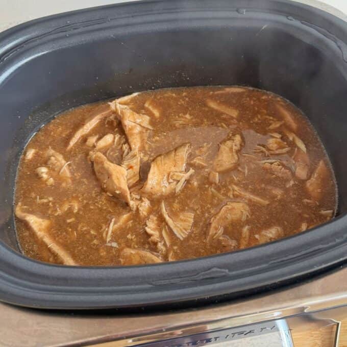 Slow Cooker Asian Style Chicken Shredded meat in brown sauce cooking in a slow cooker.