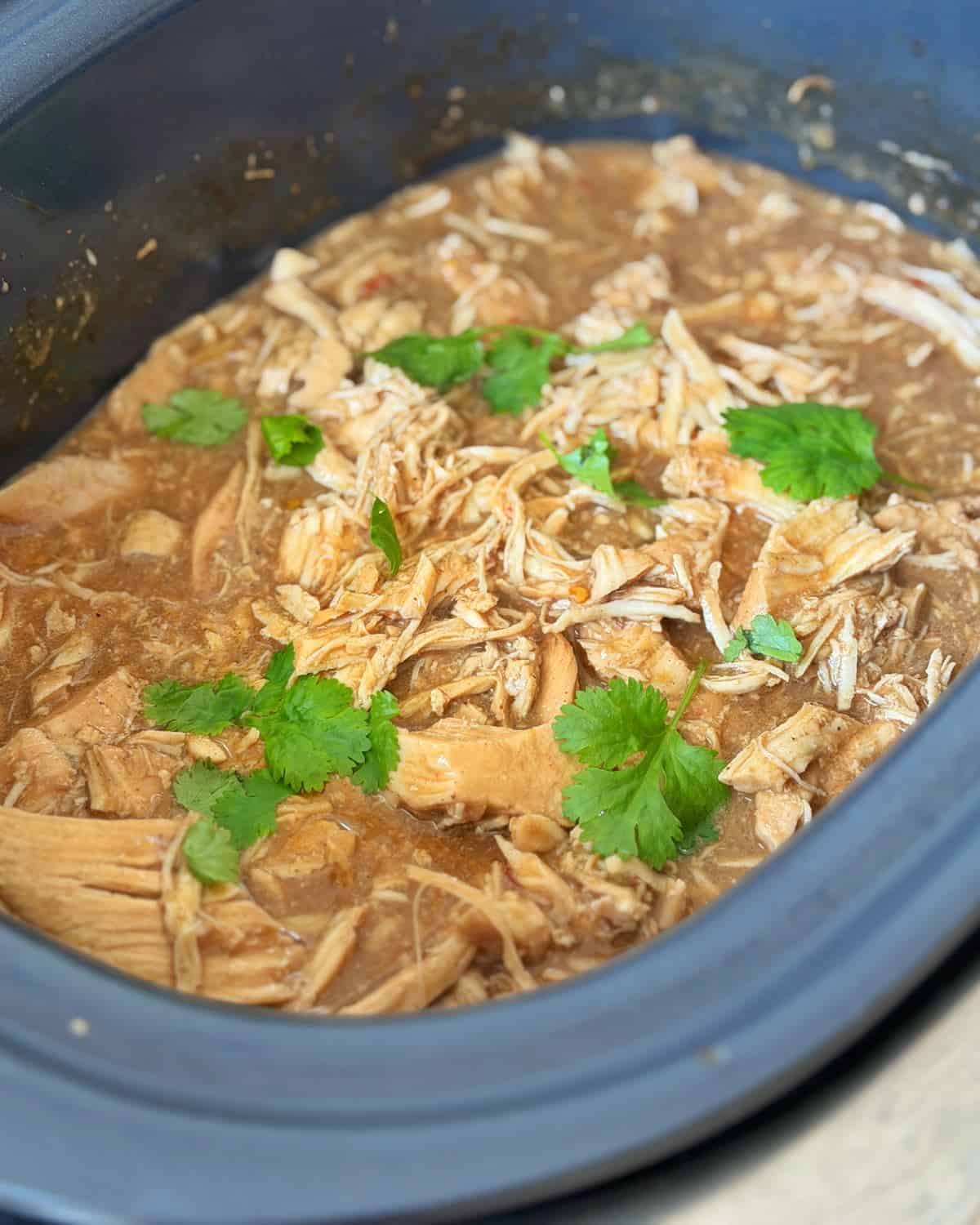 Slow Cooker Asian Style Chicken Shredded chicken in sauce garnished with fresh cilantro leaves in a slow cooker.