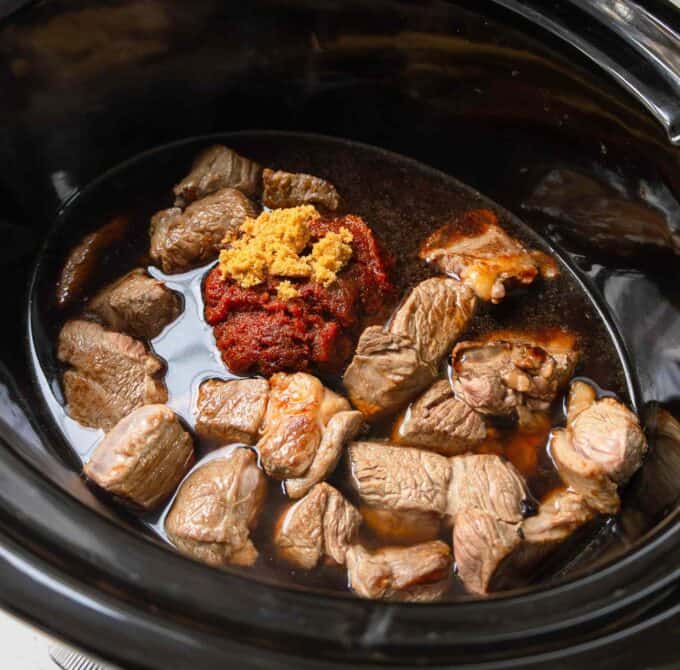 Slow Cooker Thai Beef Curry Chunks of raw beef, tomato paste, and brown sugar in a slow cooker with liquid, ready to be cooked.